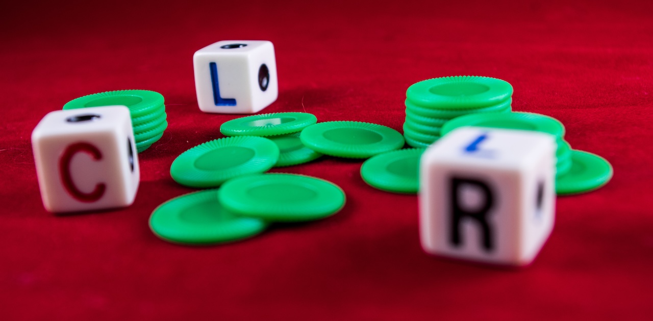 Left Center Right game dice with green chips on a red felt surface, showing C, L, and R sides.